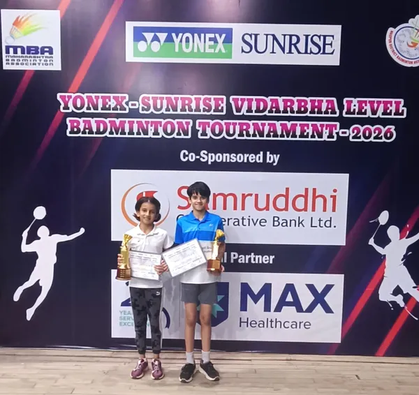 Two young students stand in front of a badminton tournament backdrop holding trophies and certificates.