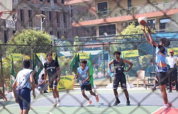 Basketball players in dark and blue jerseys on an outdoor court, photographed through a fence, with one player shooting the ball. - DPS (Mihan)