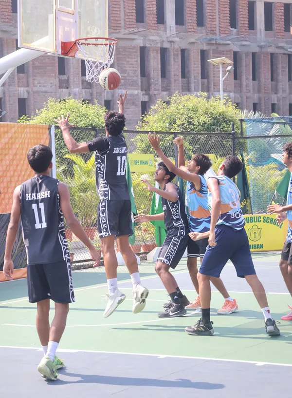 Players in dark and blue jerseys jumping for the ball near the basket on an outdoor court. - DPS (Mihan)