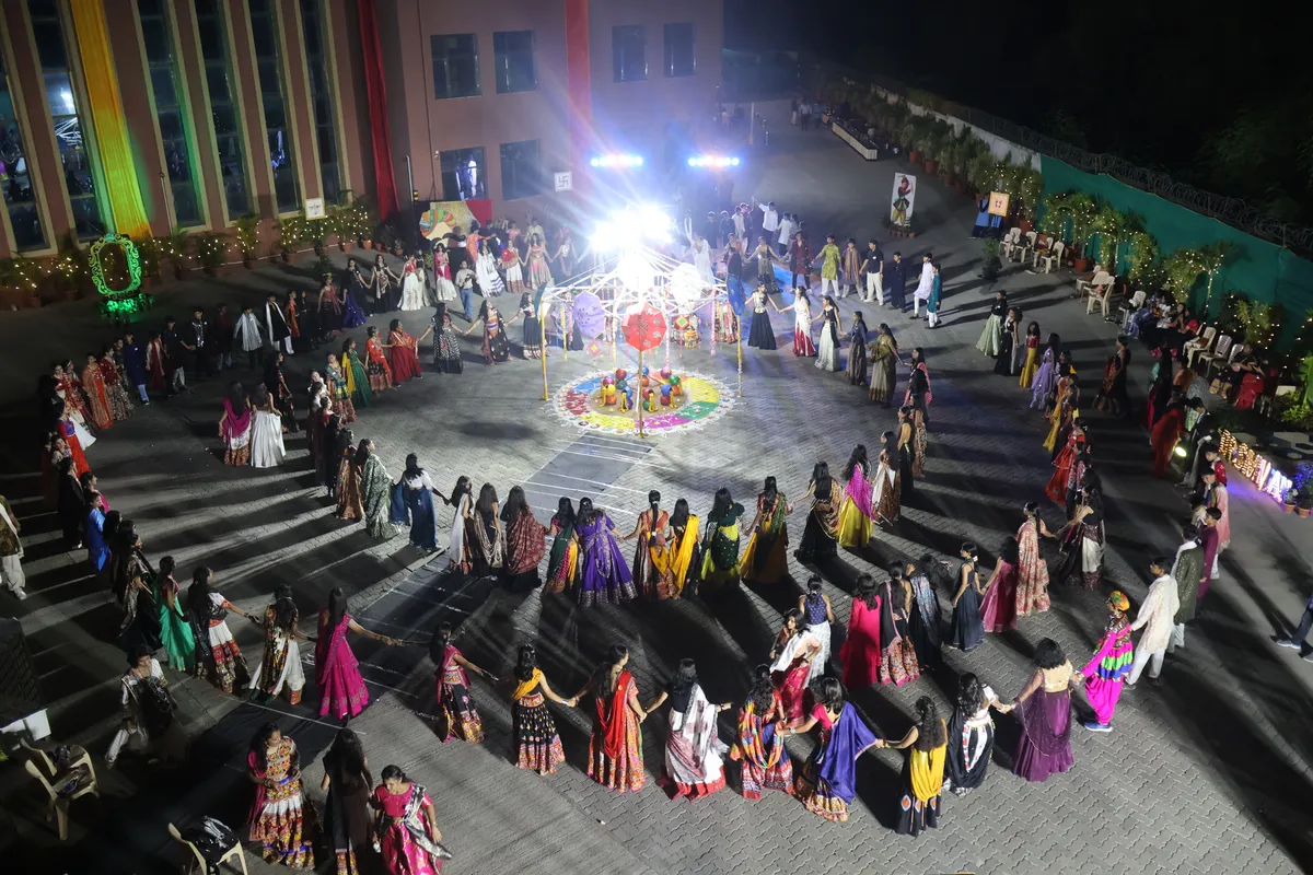 Aerial night view of many people in traditional dress dancing in a large circle around a decorated central structure in a courtyard. - DPS (Mihan)