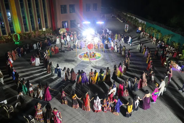 Aerial night view of many people in traditional dress dancing in a large circle around a decorated central structure in a courtyard. - DPS (Mihan)