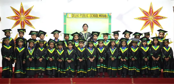Group of young children in black graduation gowns and caps with a woman at DPS (Mihan).