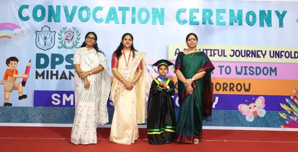 Three women on stage with a young child in graduation gown and cap at DPS (Mihan) convocation ceremony.