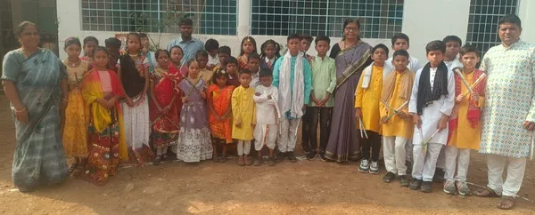 Group photo of students in traditional clothes, some holding sticks, standing with several adults in front of a school building. - Ekatmata Upper Primary School