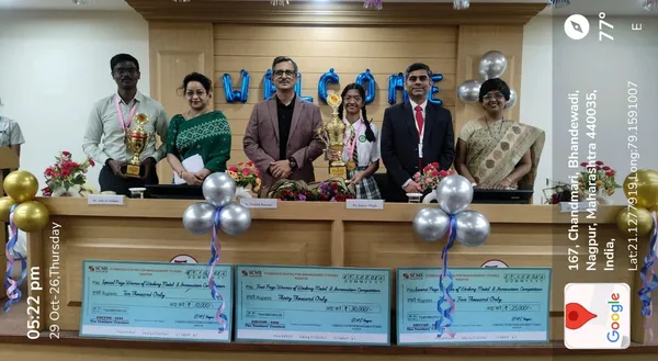 Five adults and a student pose behind a counter with trophies, balloons and three large prize cheques in front, with a GPS overlay on the side. - J. N Tata Parsi