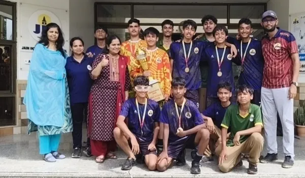 Jain International Boys' Futsal Team group photo with students in sports uniforms, medals, and trophy with adults outside school building