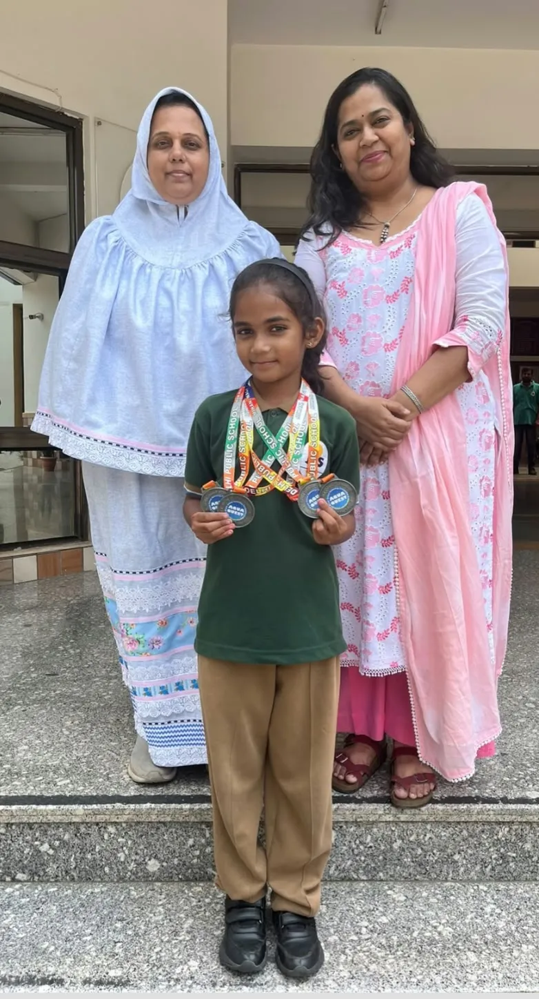 A young girl in school uniform holding several medals on colorful ribbons, standing between two women on school steps.