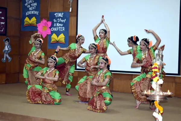 Six girls in classical dance costumes performing on a stage at Narayana Vidyalayam.