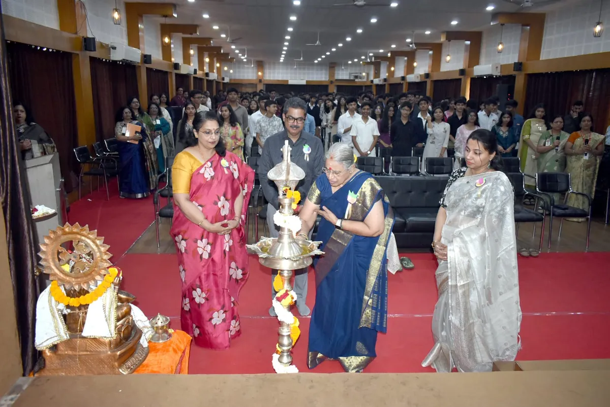 Three women and a man lighting a ceremonial lamp on a stage in front of a seated audience at Narayana Vidyalayam.