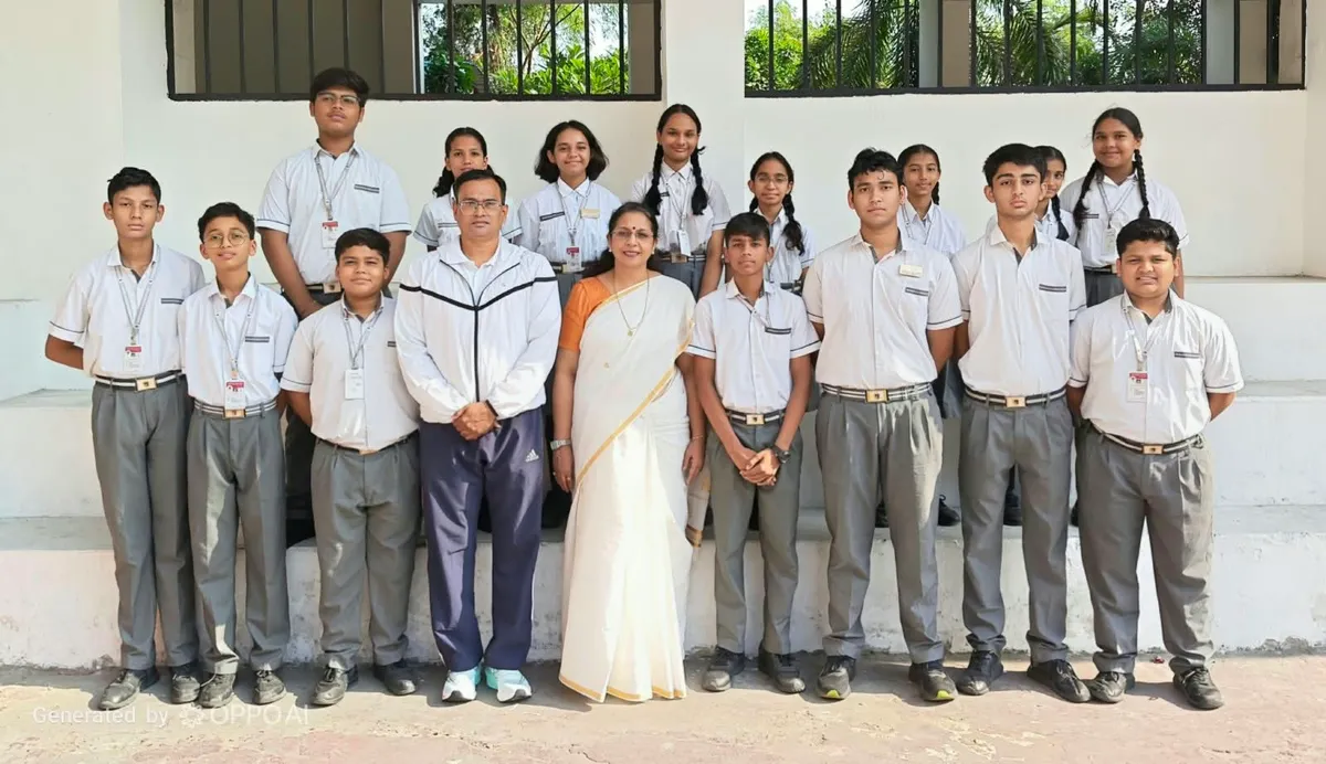 Group photo of about 15 students in school uniforms standing in rows with a man in a tracksuit and a woman in a saree in front of a building. - Narayana Vidyalayam