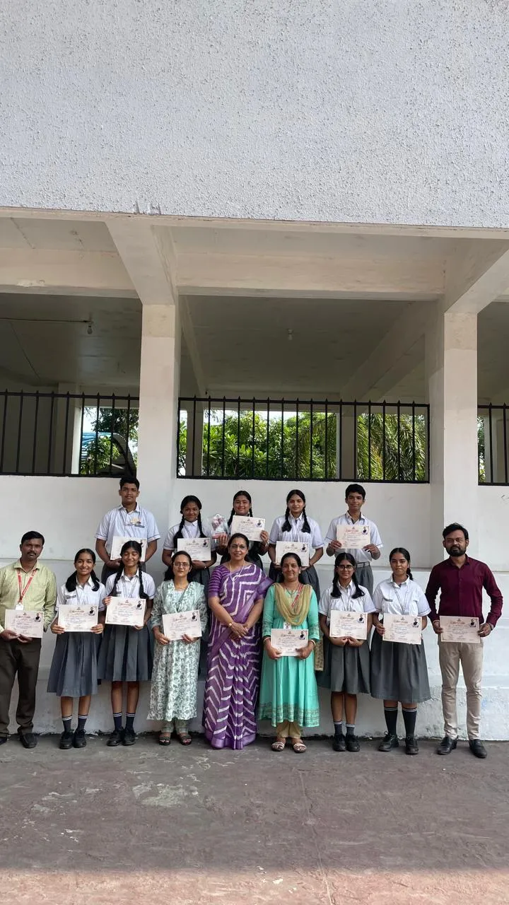 Group photo of students and teachers standing in two rows outdoors in front of a building, with most holding certificates.