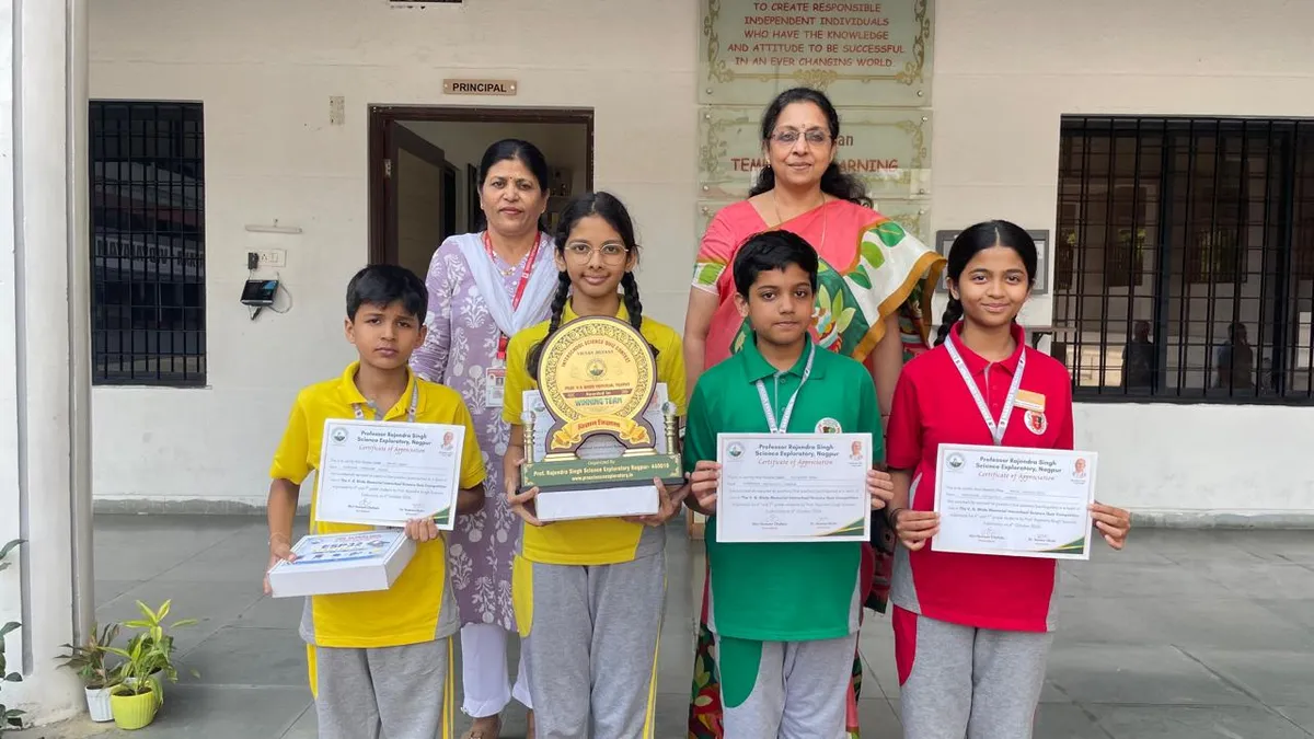 Four students holding a trophy and certificates pose with two women teachers in front of a school building. - Narayana Vidyalayam