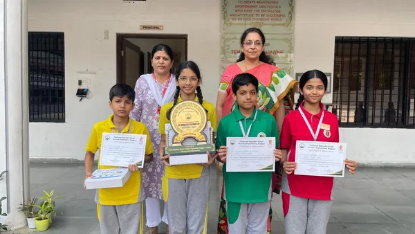 Four students holding a trophy and certificates pose with two women teachers in front of a school building. - Narayana Vidyalayam