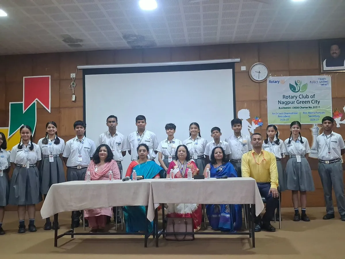 Group photo of Narayana Vidyalayam students in uniform standing in a row behind a table where five adults sit, in a hall with a projector screen and a Rotary banner on the wall.