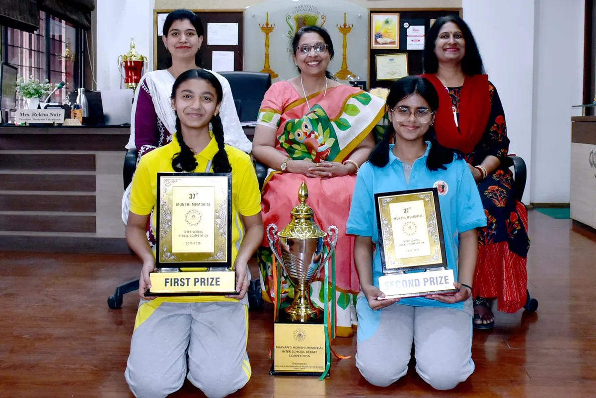 Two girls kneeling with prize plaques and a trophy in front of three smiling women seated and standing in an office. Narayana Vidyalayam.