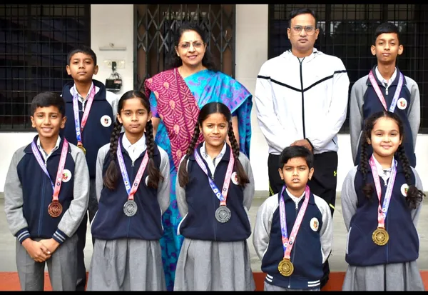 Group photo of six students wearing medals on ribbons, posing with a woman and a man in front of a building.
