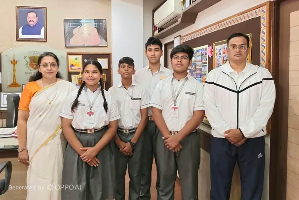 Indoor group photo of a woman in a saree, four students in school uniform and a man in a white jacket posing in an office with framed pictures on the walls. - Narayana Vidyalayam