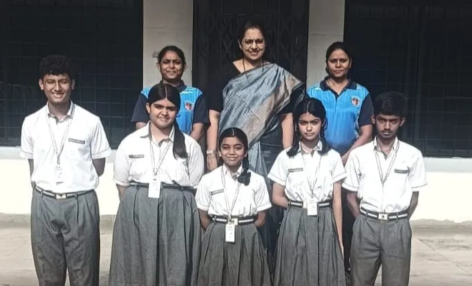 Group photo of five students in school uniforms standing in front of three women teachers outdoors against a building wall. - Narayana Vidyalayam