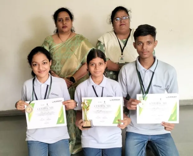 Three students holding certificates, a medal and a small trophy, with two women standing behind them, posed against a plain wall. - Sandipani (Hazaripahad)