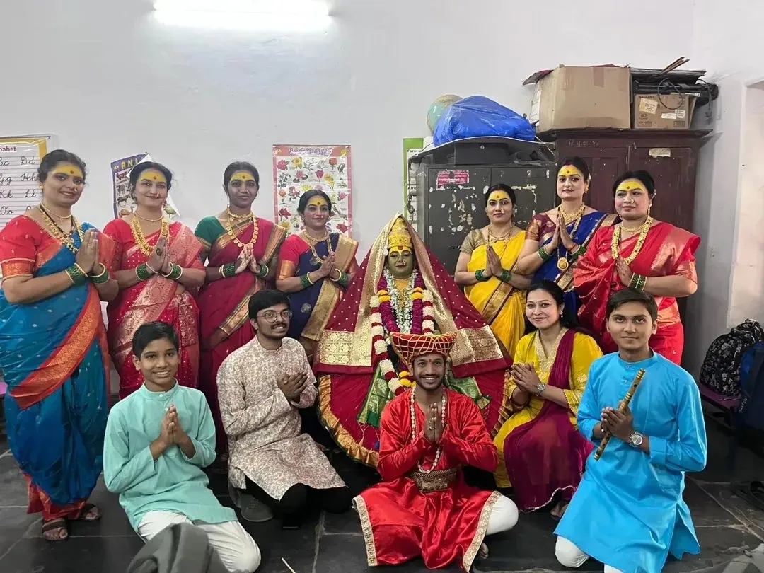 group photo of women in traditional saris and young men in ethnic dress posing around a decorated statue with garlands in an indoor room - Somalwar Nikalas
