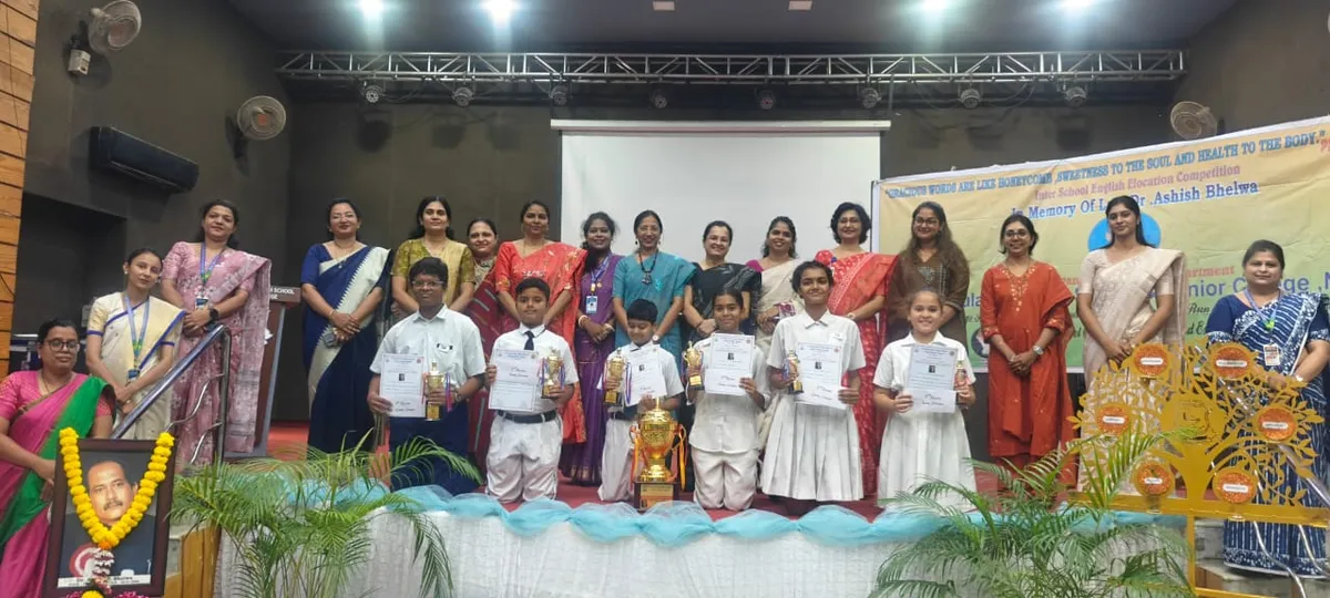 Group photo on stage of children holding certificates and trophies with women in sarees standing behind them at St. Ursula Girls' High School & Jr. College event.