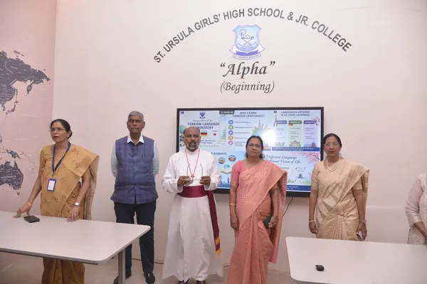 Adults including a priest in white robes standing in front of a language laboratory sign during inauguration at St. Ursula