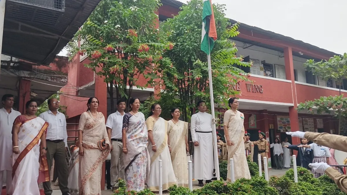 Teachers, a priest and students standing in a row near a flagpole with the Indian flag raised, in front of the St. Ursula school building.