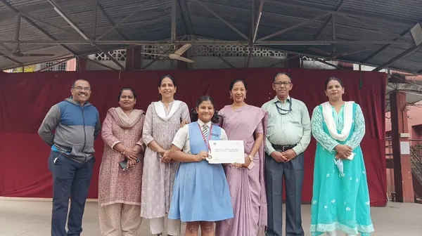 Girl in school uniform with medal and certificate standing with six adults in front of a red curtain.