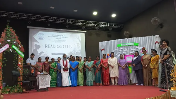 Group photo of about 20 teachers and staff standing in a row on a decorated stage in front of a projected screen for St. Ursula's reading club event.