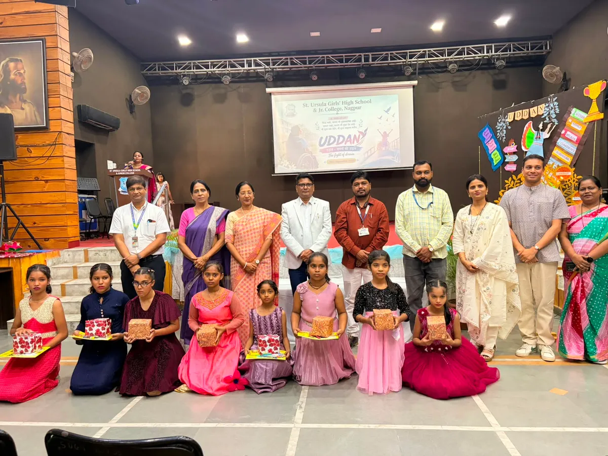 Adults standing behind girls kneeling with wrapped gift boxes on an auditorium stage at St. Ursula