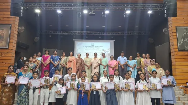 Group photo on a stage of teachers and school students holding certificates and award plaques, with a projected screen behind them. - St. Ursula