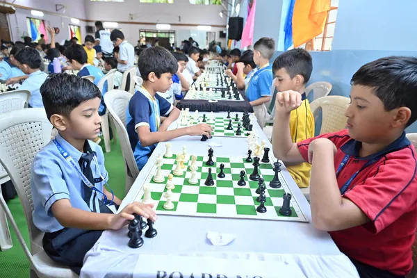 Students in school uniforms playing chess at long tables in a large hall, with rows of other players in the background at St. Vincent Pallotti.