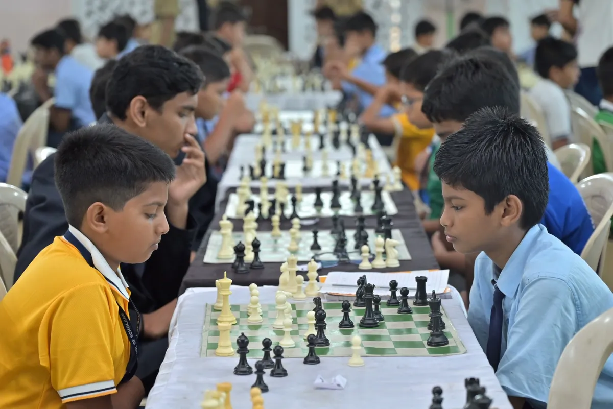 Two school boys concentrating on a chess game in the foreground, with many other players seated at chess tables behind them at St. Vincent Pallotti.
