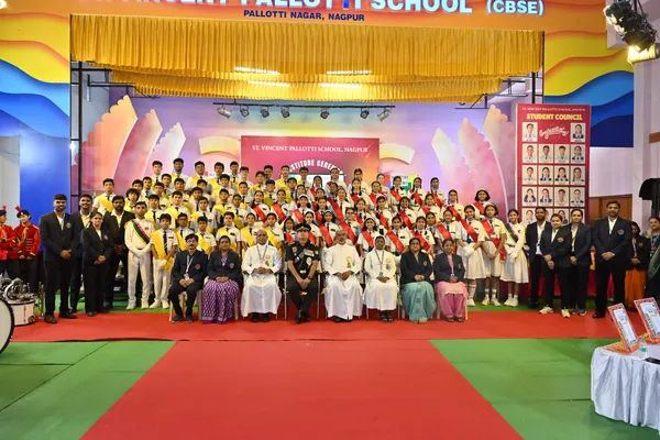 Wide group photo of many students in sashes with seated guests and staff on a decorated stage, with a student council board on the right. - St. Vincent Pallotti