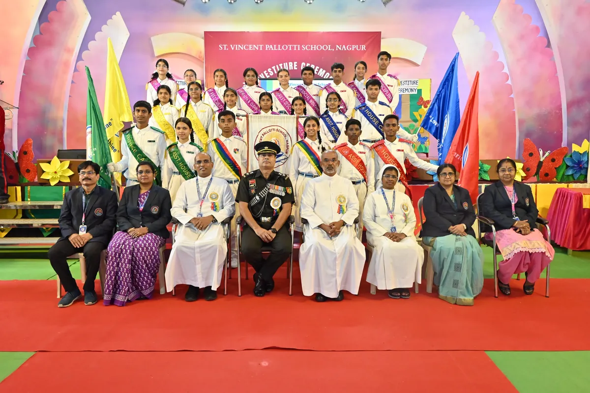 Sharp group photo of students wearing sashes standing behind seated dignitaries and clergy on a decorated stage with flags and a red carpet. - St. Vincent Pallotti