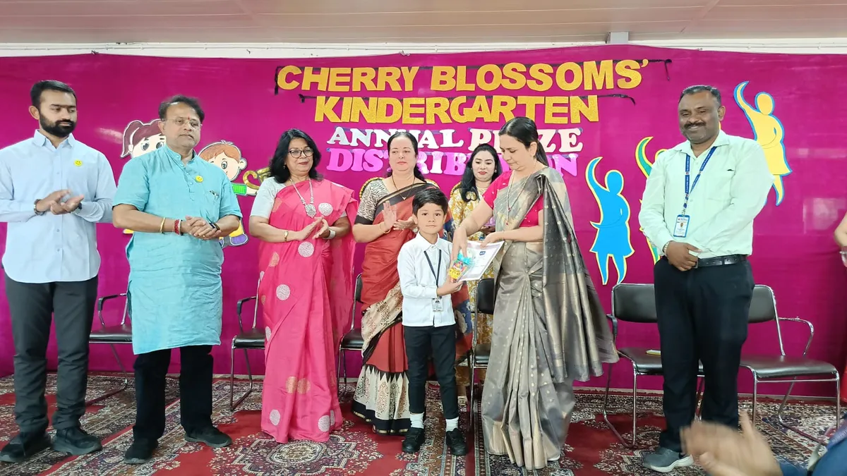 Stage photo of a woman handing a prize to a young boy, with five adults standing and applauding in front of a pink prize distribution banner at The South Public School.