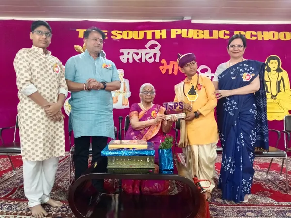 The South Public School event: people pose on stage with elderly woman and gifts against magenta school banner.